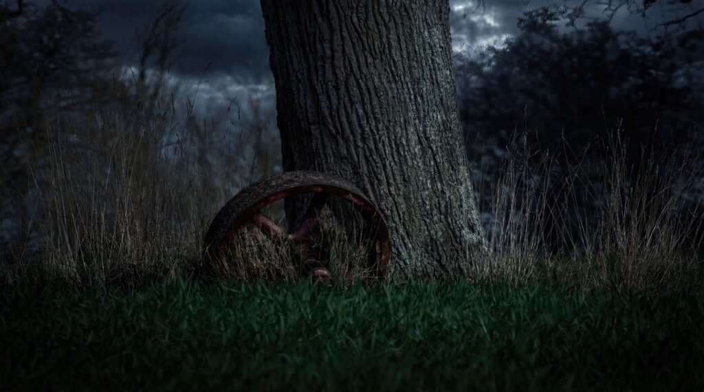 A rusted iron wheel resting against an old tree trunk under a brooding stormy sky.