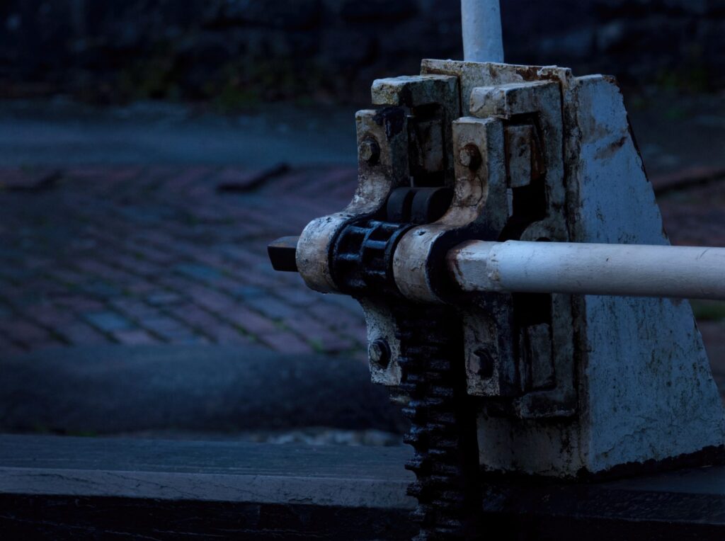 A macro study of industrial heritage. The weathered textures and heavy iron of a lock gate mechanism stand in cold, silent focus, representing the enduring stre...