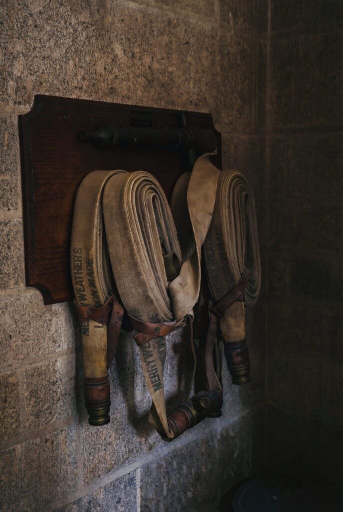 Coiled fire hoses hang in quiet readiness against cold stone walls, leather straps worn by time and service