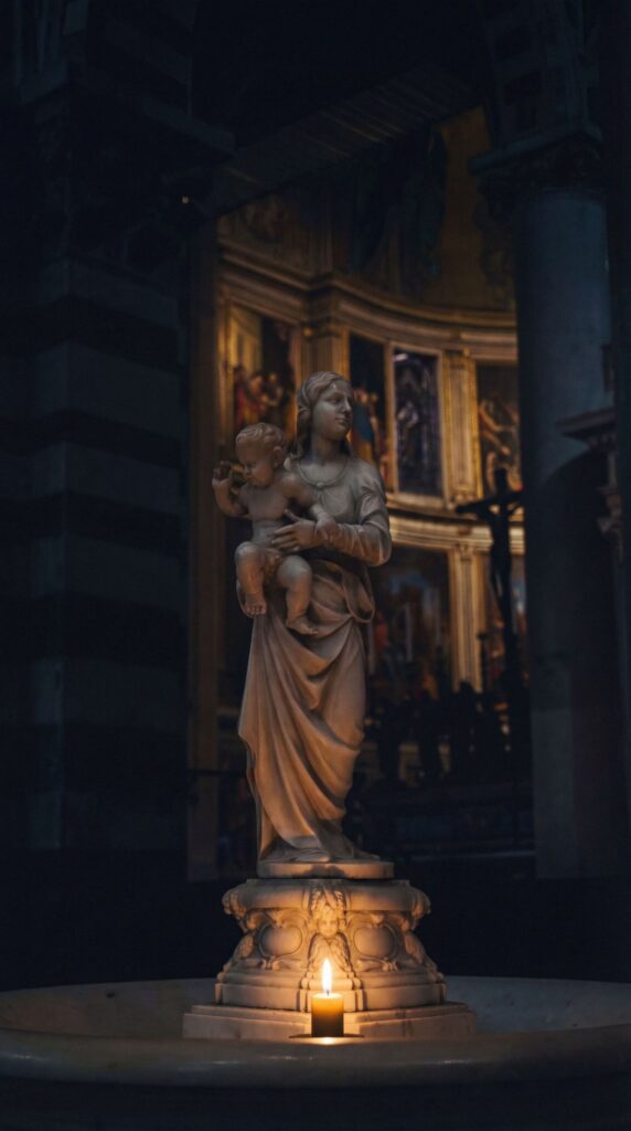 A religious statue illuminated by candlelight in a dark church interior creates a dramatic atmospheric scene.